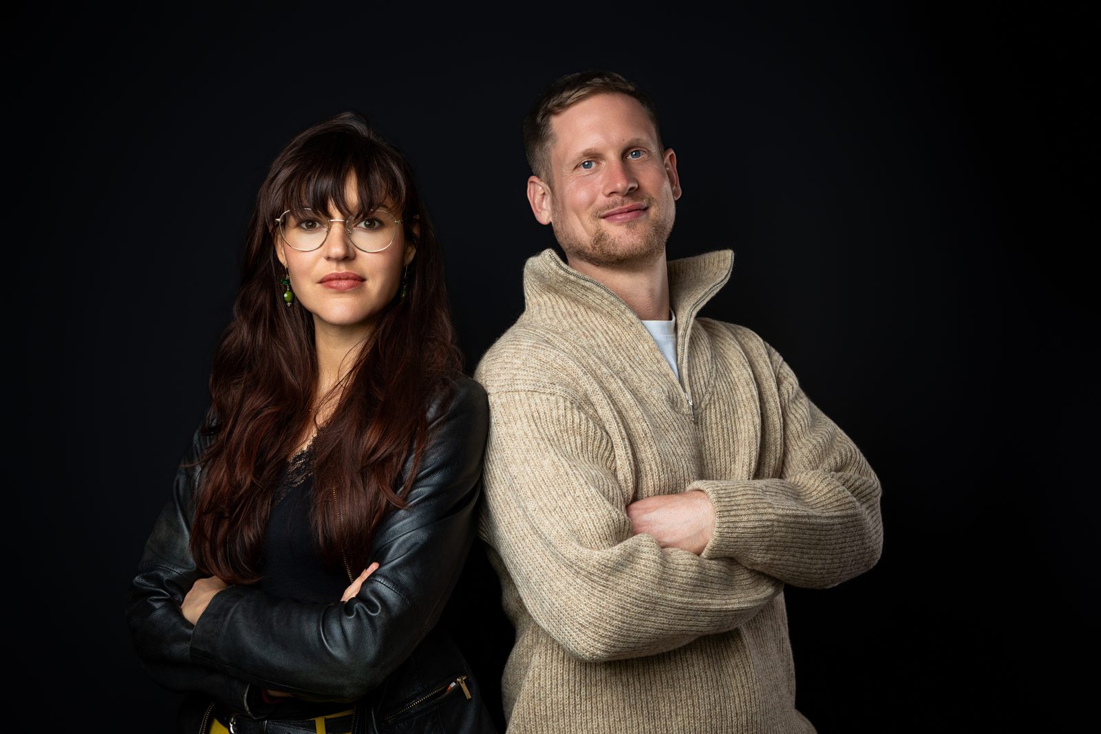 Ronja und Clemens stehen selbstbewusst nebeneinander vor dunklem Studiohintergrund